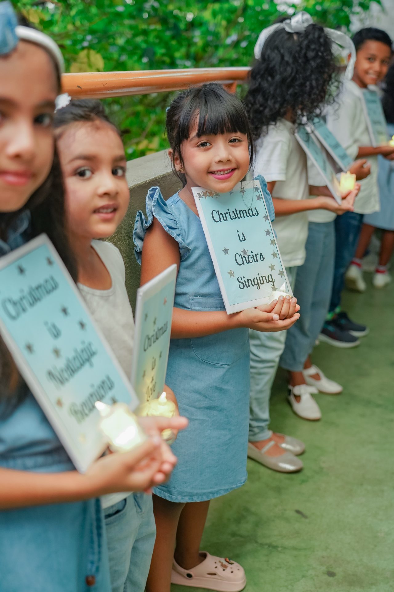 Children in blue holding certificates outdoors at a joyful Christmas-themed event.