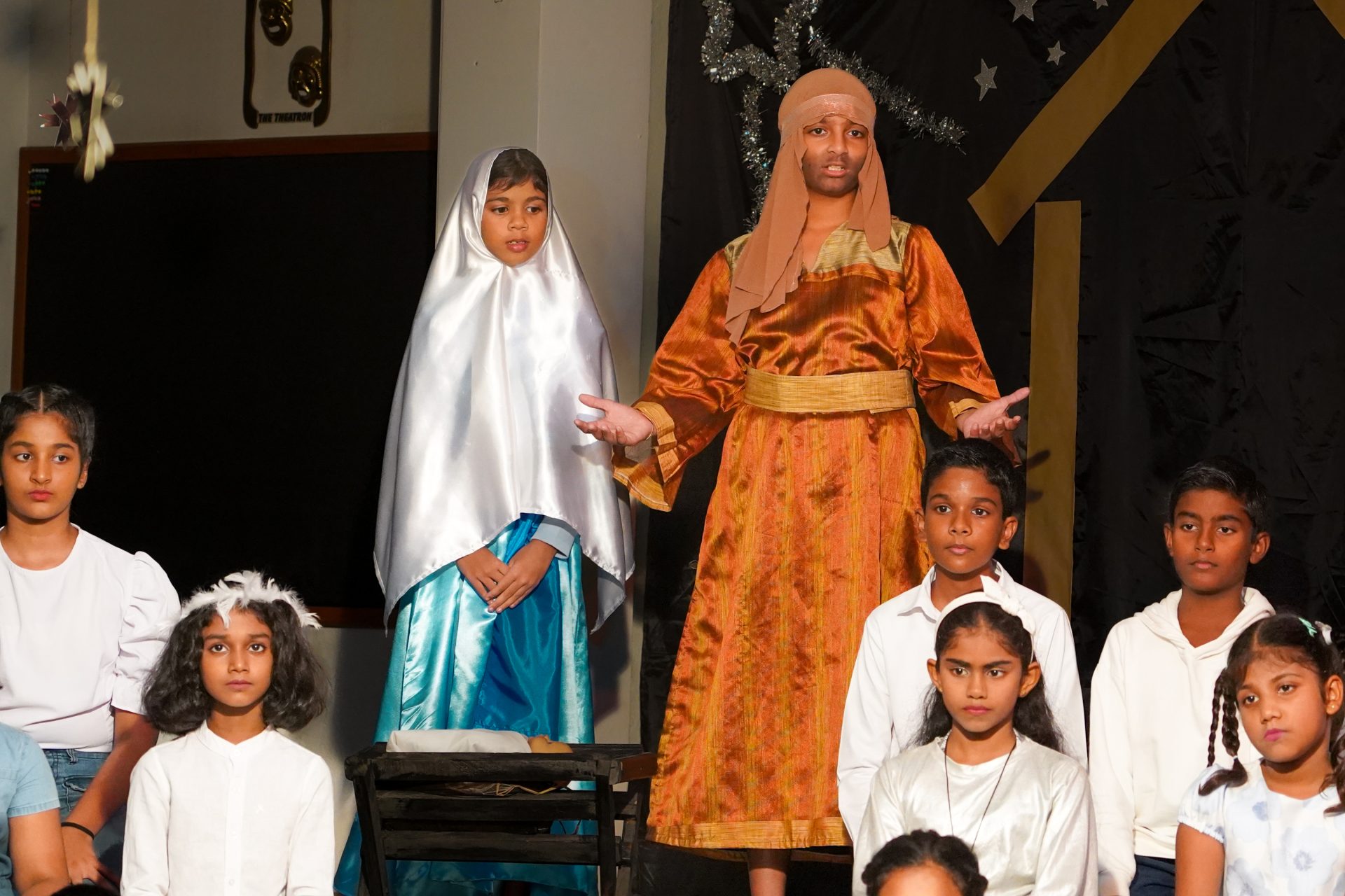 Childrens nativity play with Mary, Joseph, angels; festive, community performance, starry backdrop.