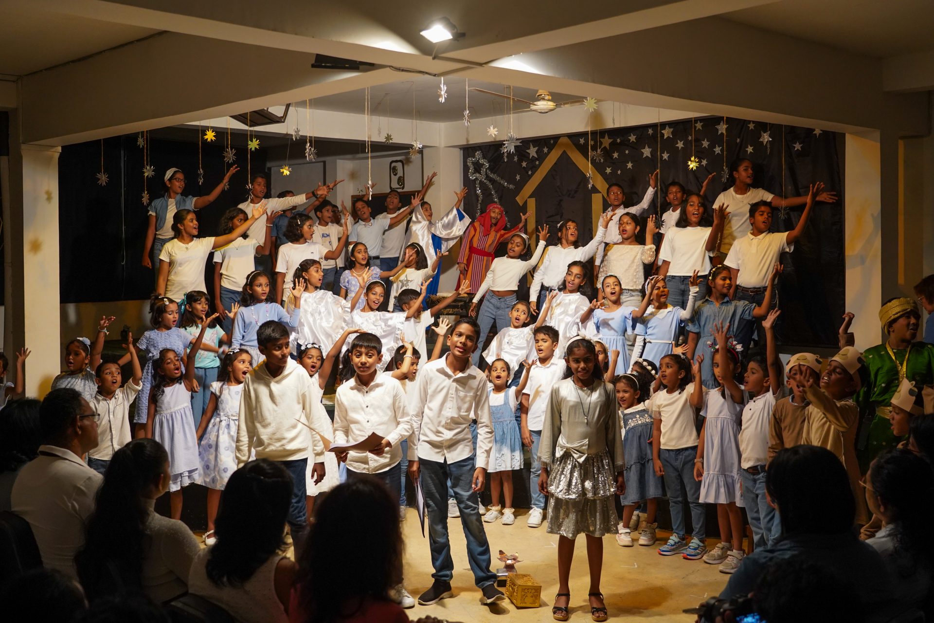 Childrens choir performs energetically on stage with festive decorations and engaged audience.