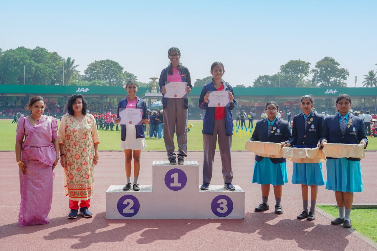 Outdoor athletic awards ceremony with podium winners, vibrant organizers, students holding gifts.