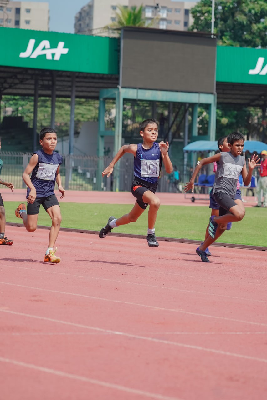 Four boys sprinting vigorously on track in urban sports facility, showcasing focus and competitive spirit.