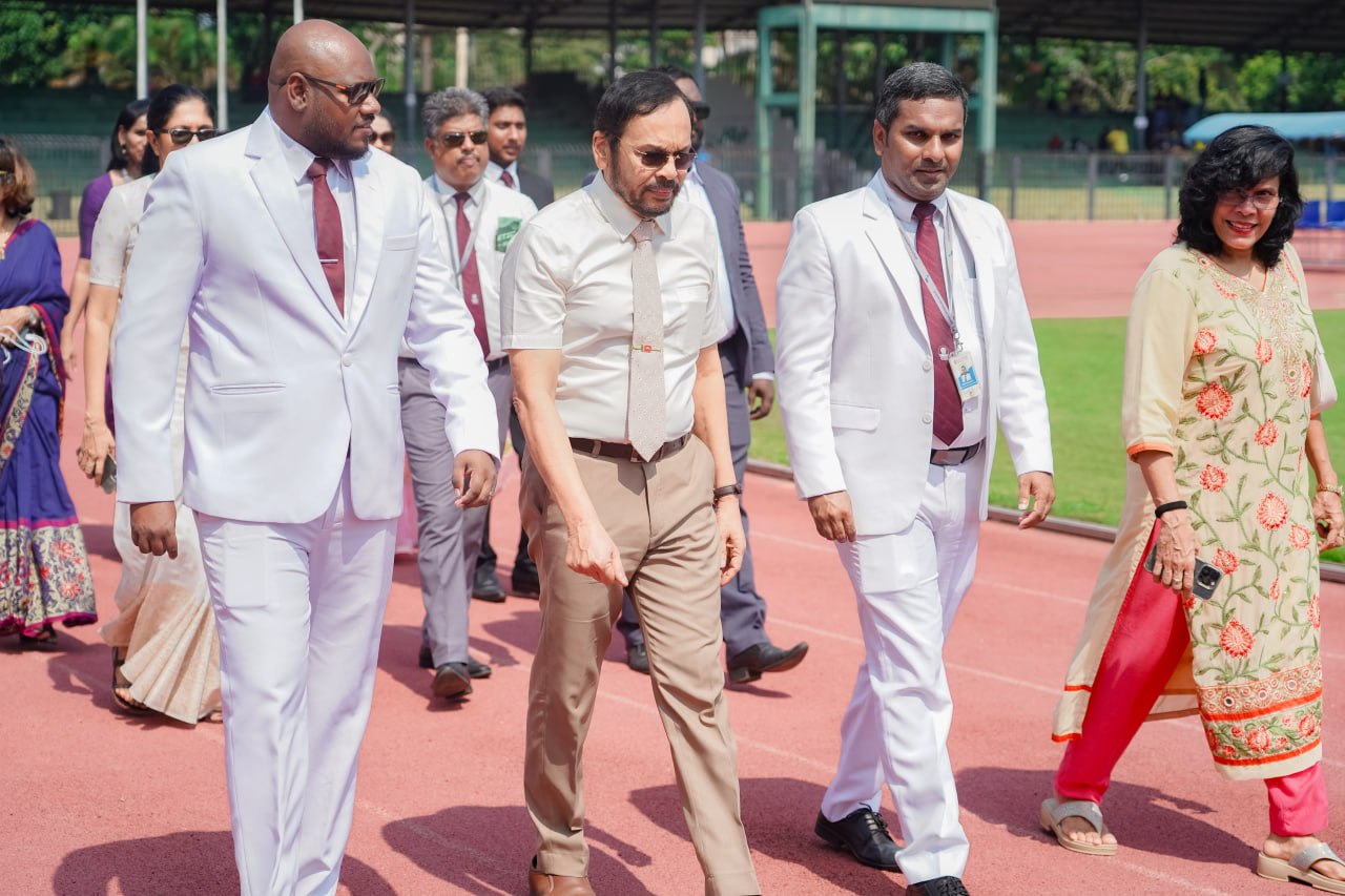 Outdoor formal event: officials in suits and a woman in floral attire on a sports track.