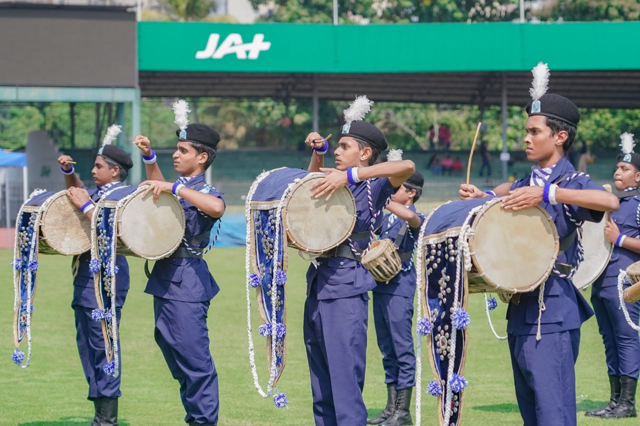 Young musicians in blue uniforms perform a synchronized drum routine outdoors.