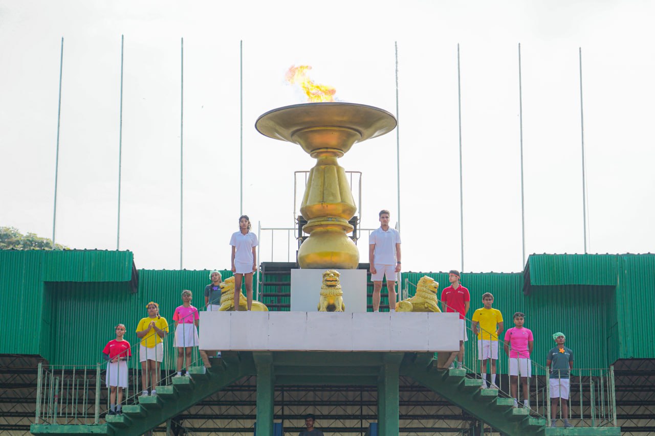 Golden cauldron with flame, colorful outfits, lion statues, unity-themed ceremony under cloudy sky.