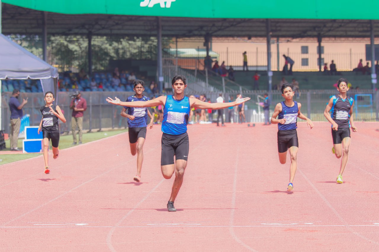 Triumphant male sprinter wins race, crossing finish line with arms outstretched at track event.