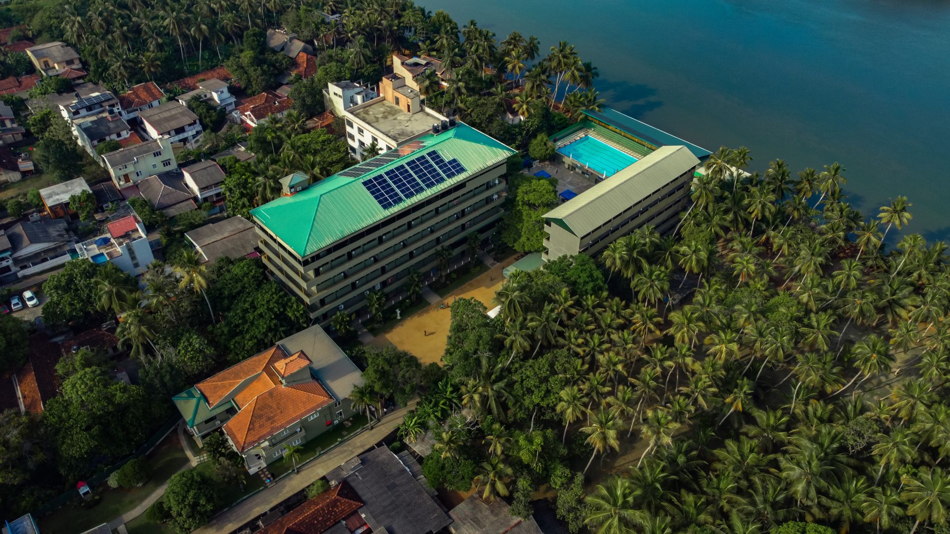 Aerial view of eco-friendly urban area with solar building, greenery, pool, and waterway.