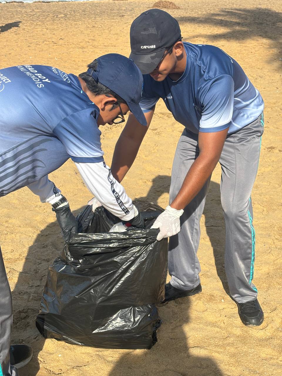 Volunteers cleaning a sunny beach in blue uniforms for environmental conservation.