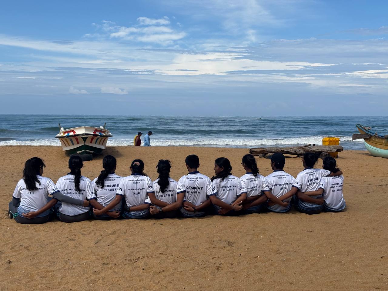 Team unity on a sunny beach with matching shirts, boats, and serene ocean backdrop.