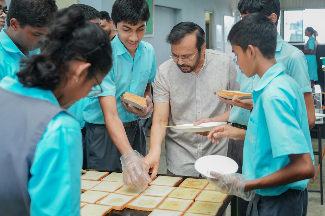 Students in blue uniforms making bread under teachers guidance in a bright classroom setting.