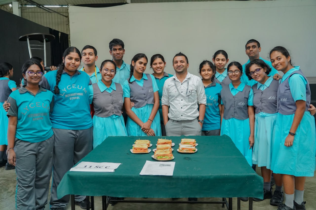 Students in uniforms present creatively stacked sandwiches for a school culinary project.