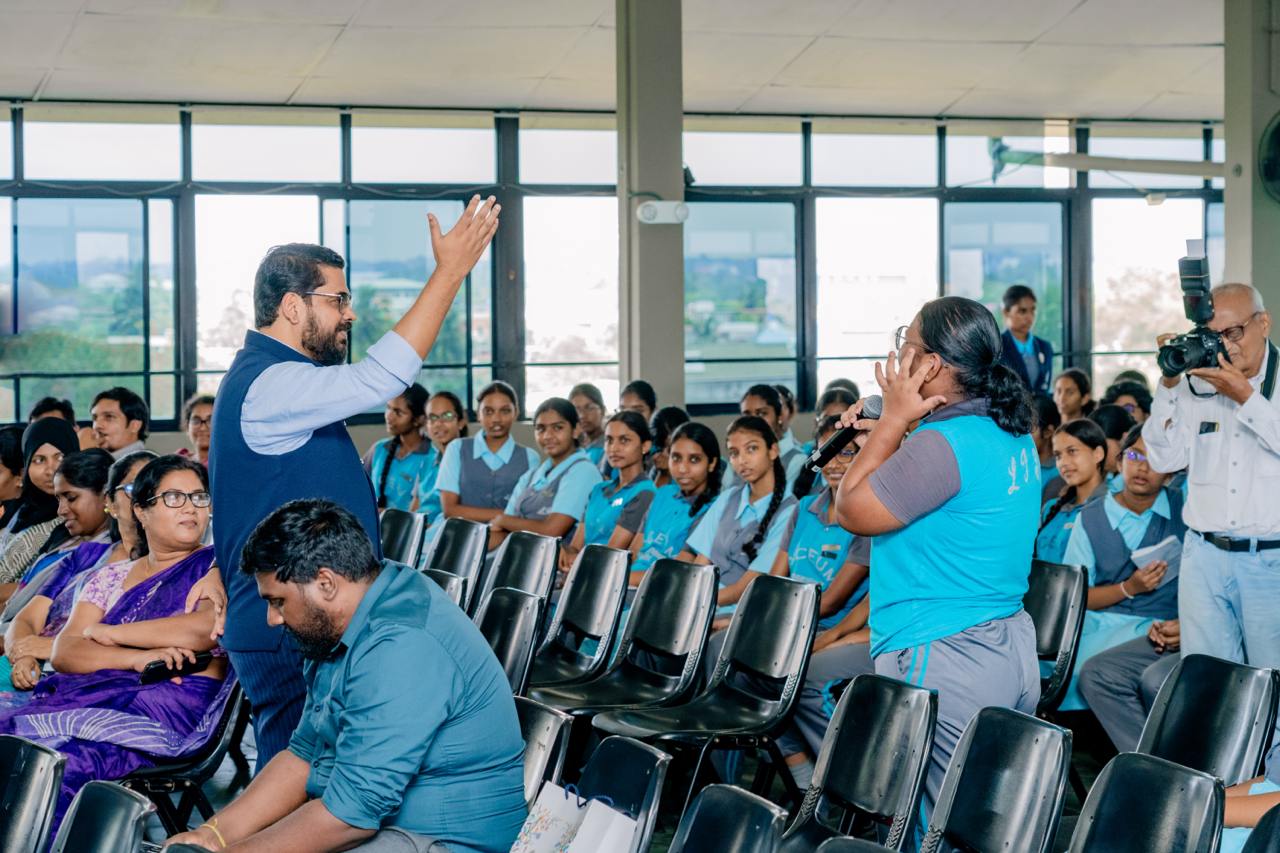 Speaker engages diverse audience in modern seminar room with urban views.