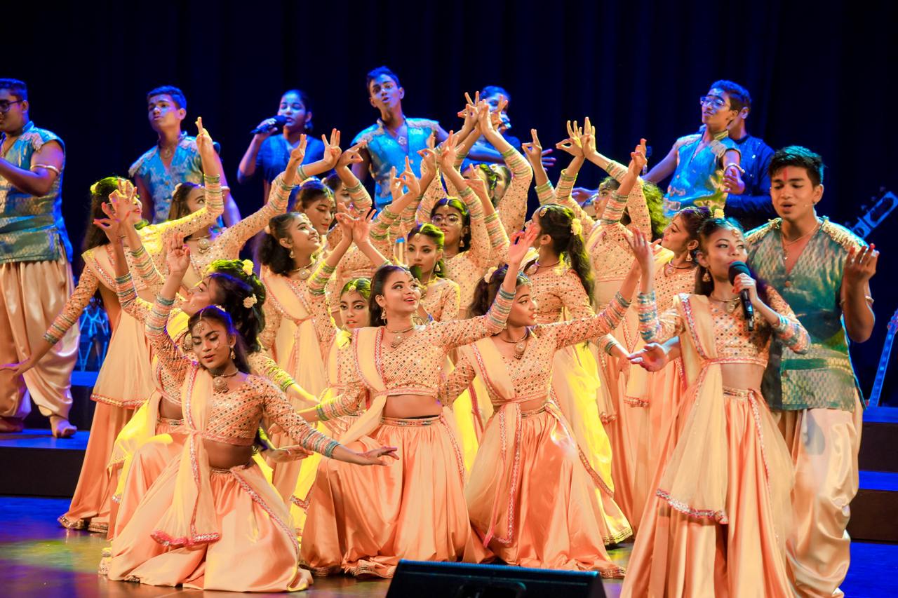 Youthful traditional dance in vibrant costumes with live music on stage.
