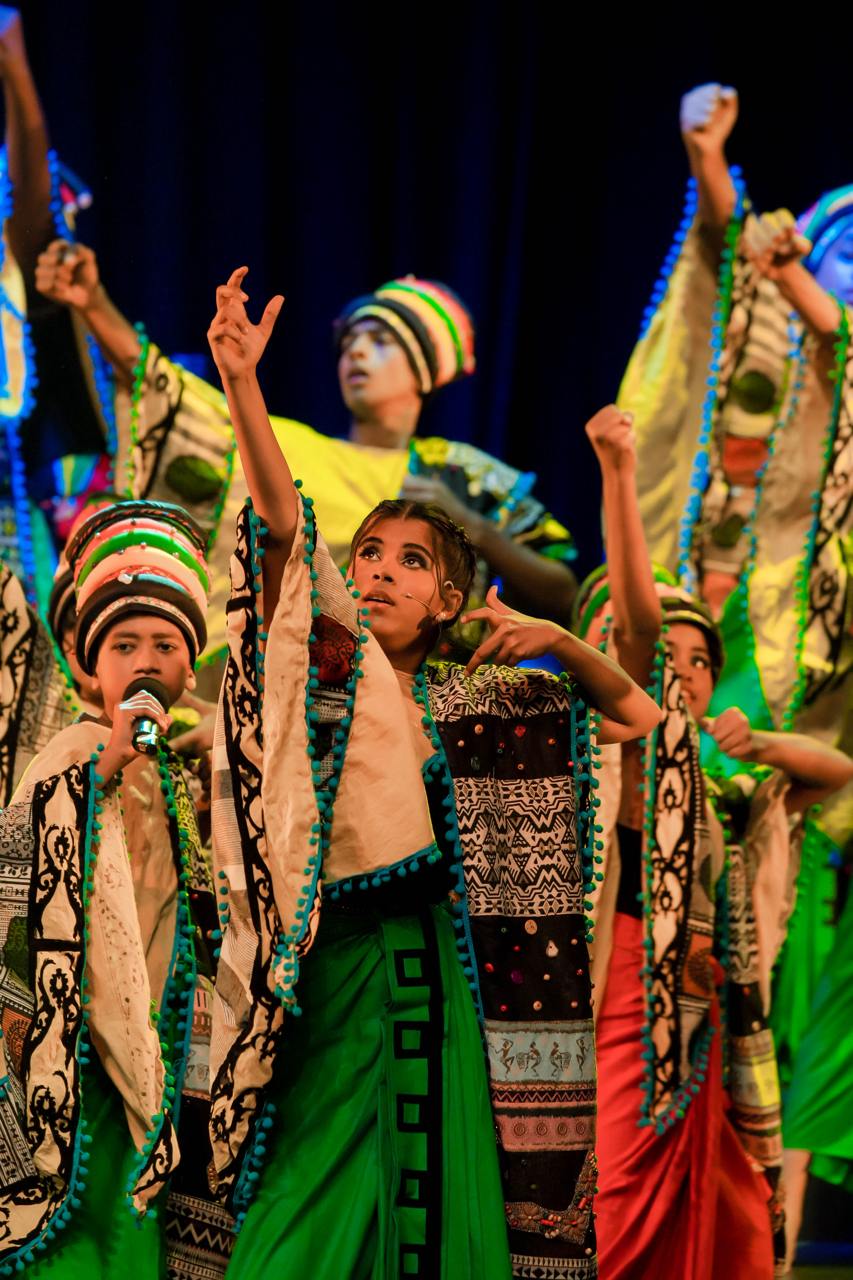 Dynamic cultural dance with vibrant costumes and expressive performers in illuminated spotlight.