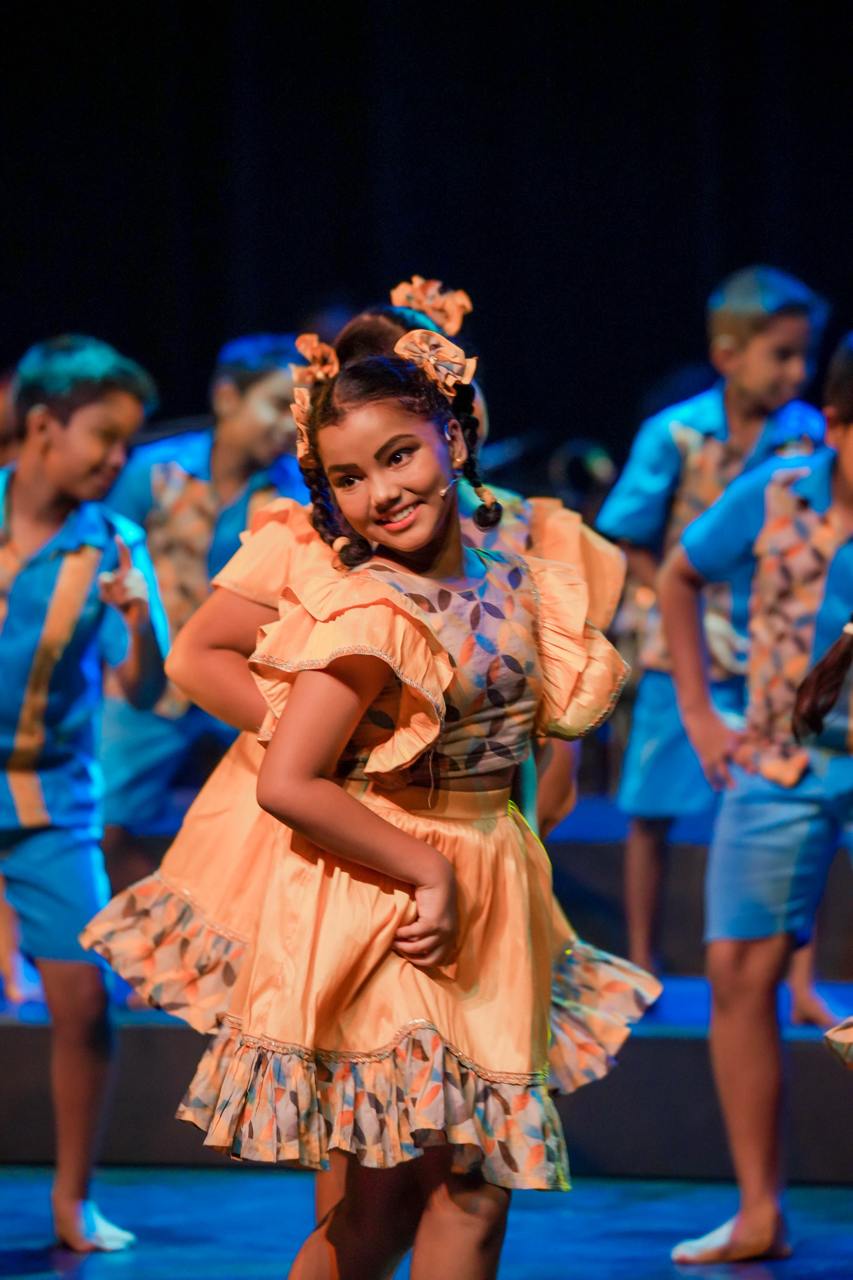 Young girl in vibrant traditional costume performing joyful cultural dance on stage.