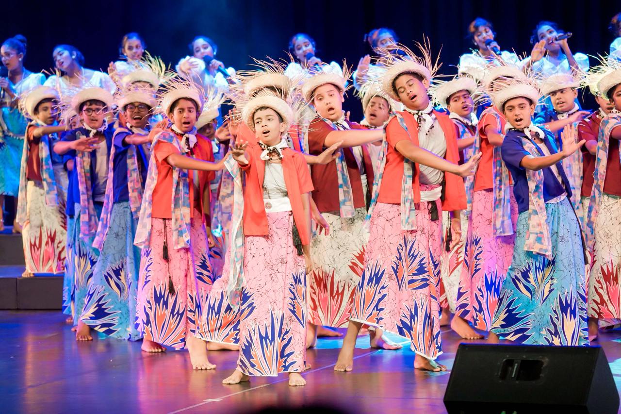 Children in colorful costumes energetically perform a traditional dance with vibrant lighting.