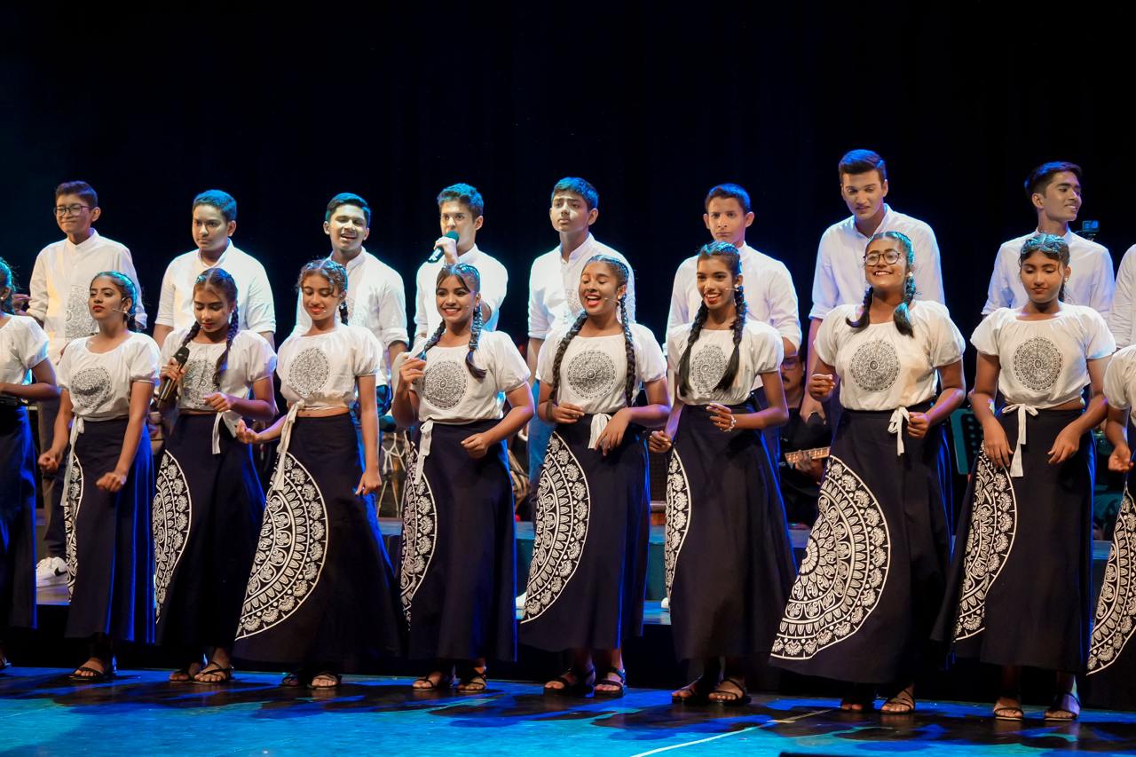 Youth perform cultural dance in vibrant attire under dramatic stage lighting.