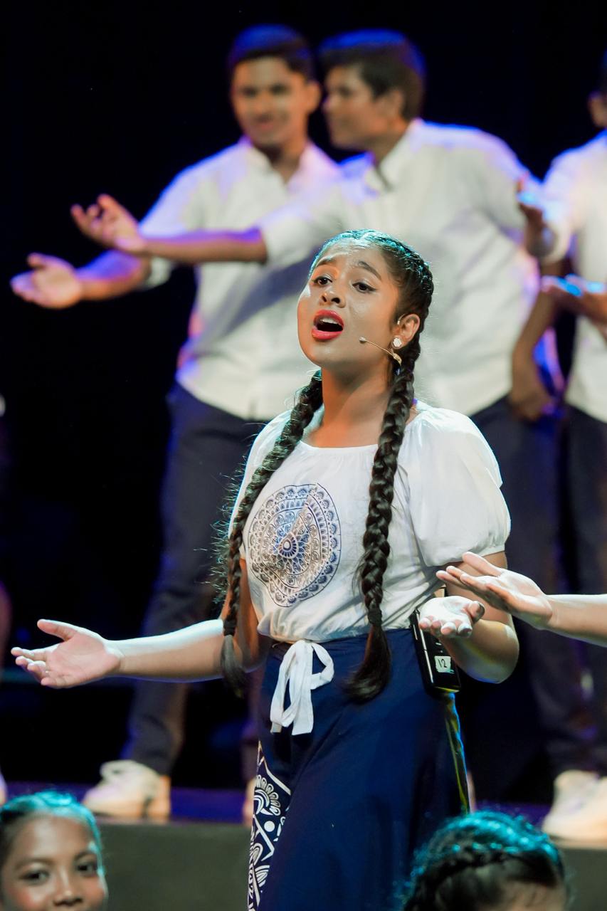 Young woman in traditional attire passionately performs on stage with energetic group choreography.