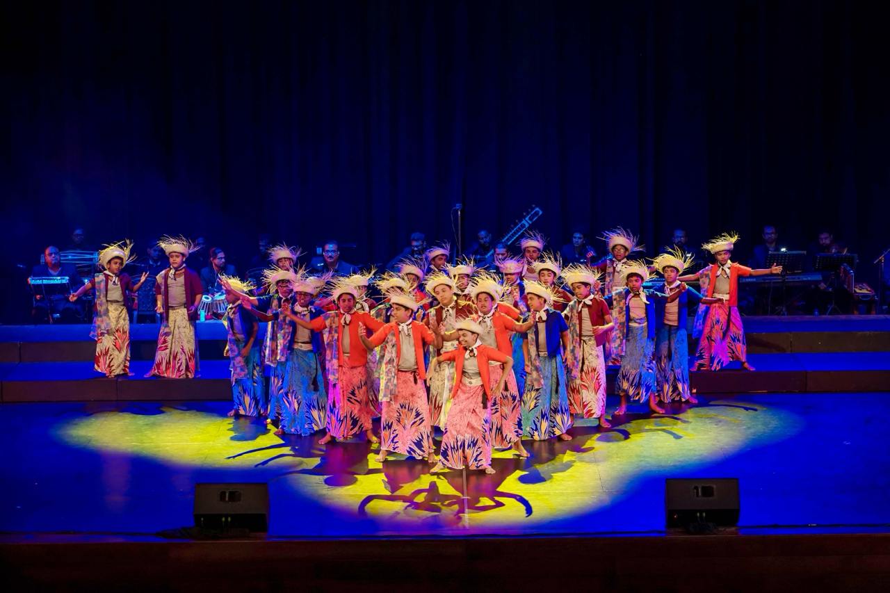 Vibrant dancers in traditional costumes perform on stage with dynamic lighting and live music.