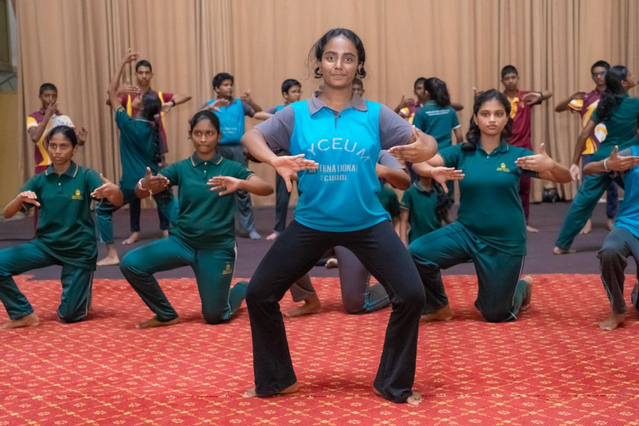 Young dancers in coordinated practice on red carpet, led by poised female instructor.