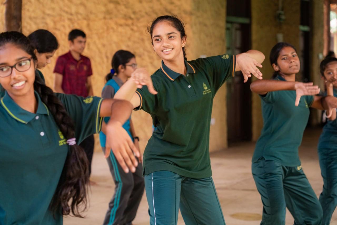 Young students joyfully practicing dance in green uniforms, highlighting teamwork and cultural diversity.
