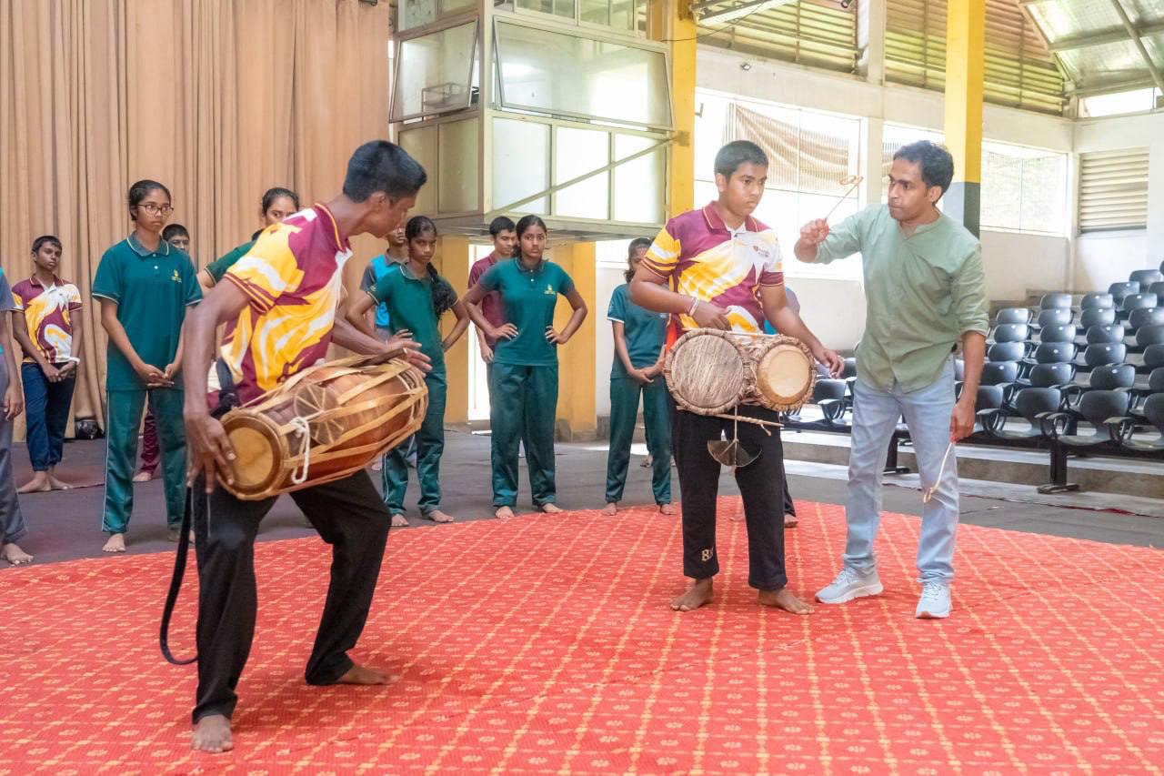 Young musicians rehearse traditional drumming under guidance in a vibrant auditorium setting.