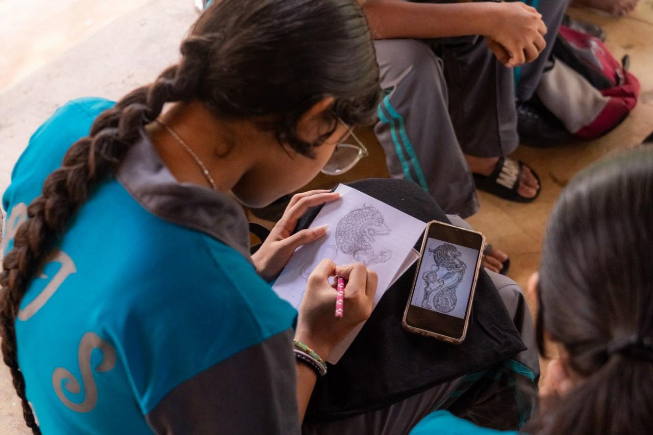 Young artist sketching with smartphone reference in a relaxed school setting.
