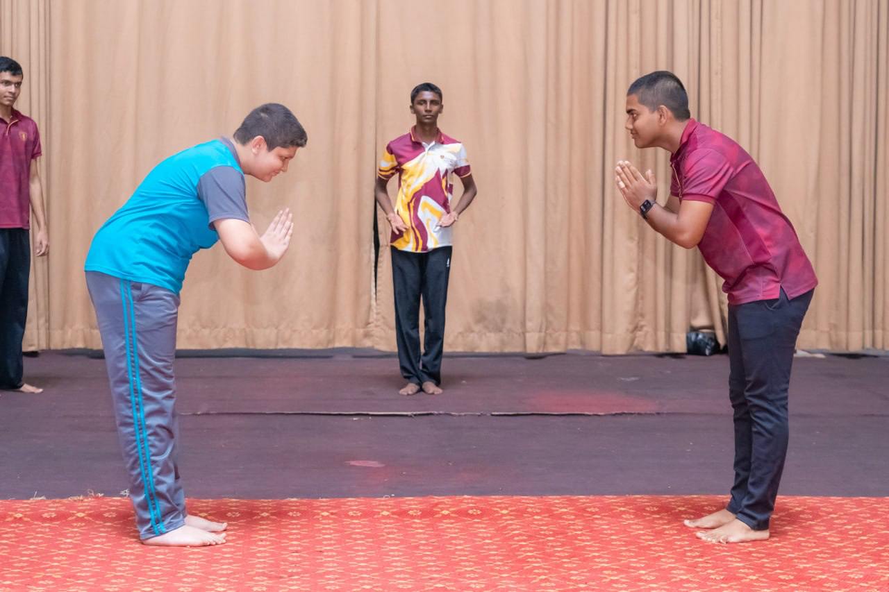 Martial arts bowing gesture on stage with instructor observing, emphasizing respect and tradition.