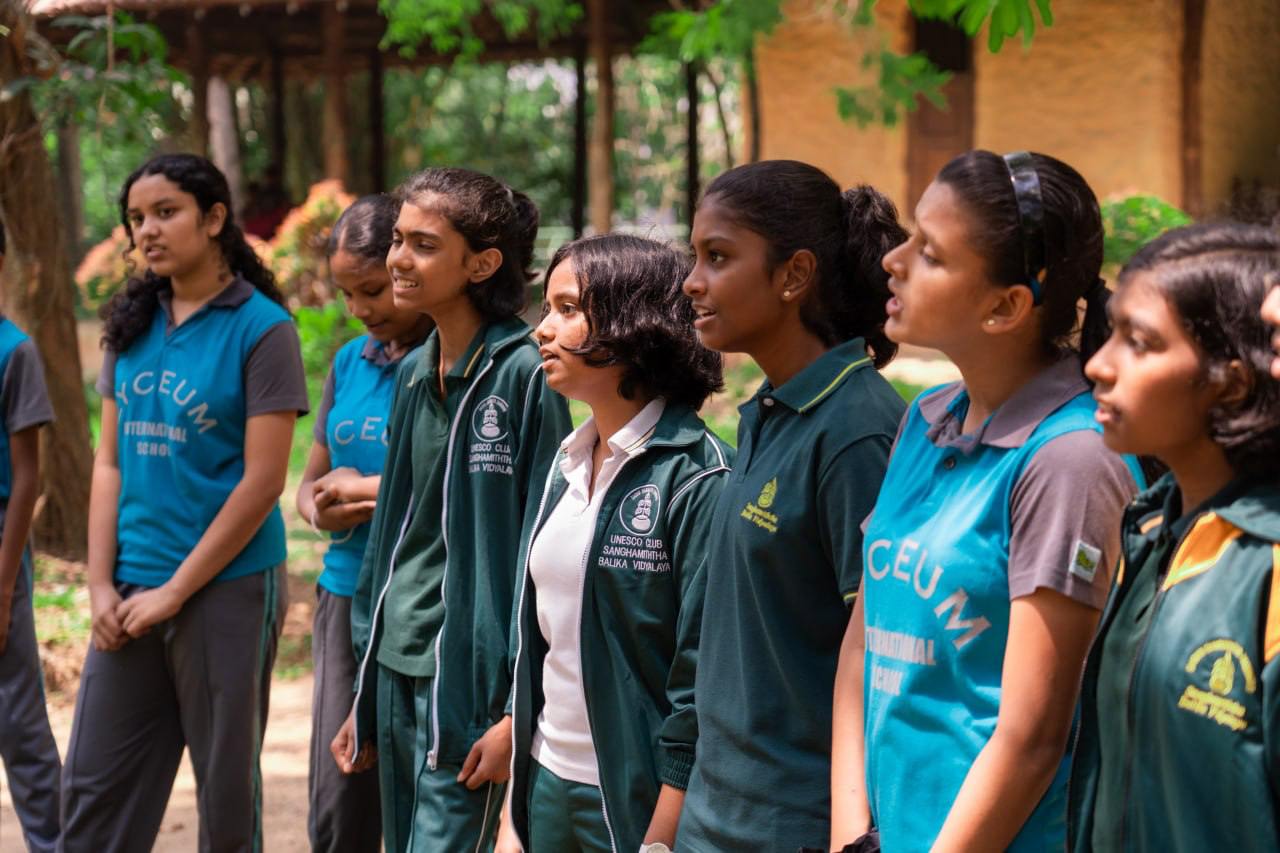 Youth in uniforms attentively await instructions in a lush park setting.