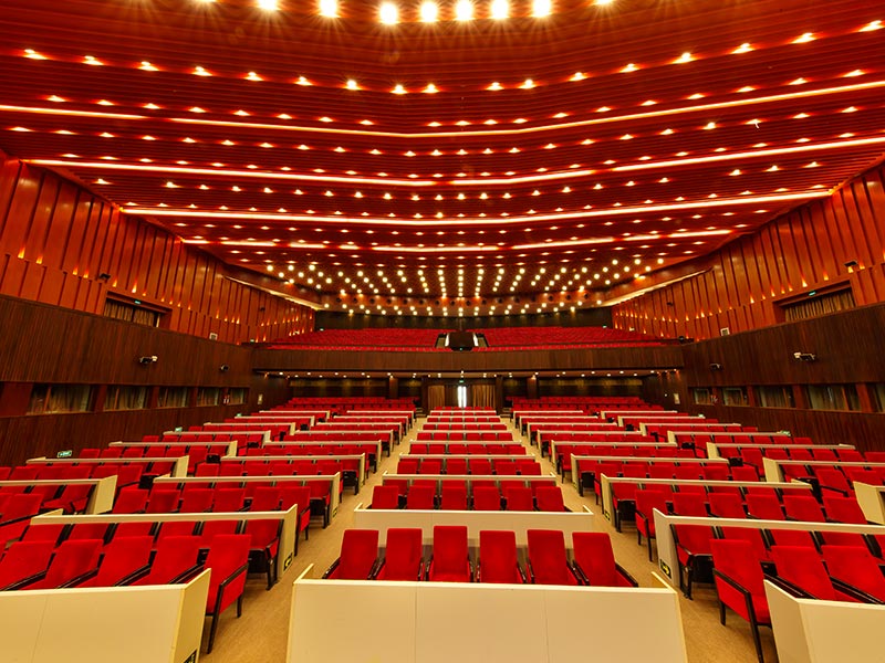 Modern Auditorium With Red Seats and Elegant Lighting Design Modern auditorium with red seats, conference hall interior, balcony, wood paneling, and stylish ceiling lights.