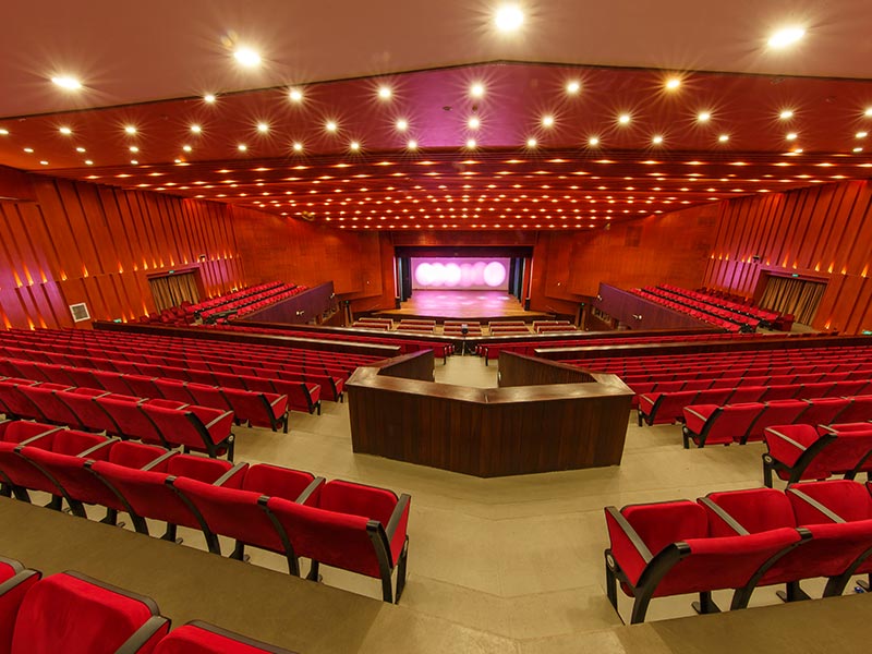 Modern Auditorium With Red Seats and Elegant Stage Lighting Modern auditorium with red seats, wooden panels, bright lighting, and stage ready for performance.