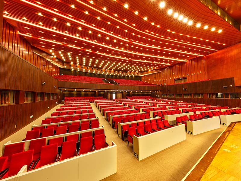 Elegant Modern Conference Hall With Red Seating and Wooden Ceiling Modern auditorium hall with red seats, elegant wood ceiling, and spacious layout for conferences or events.