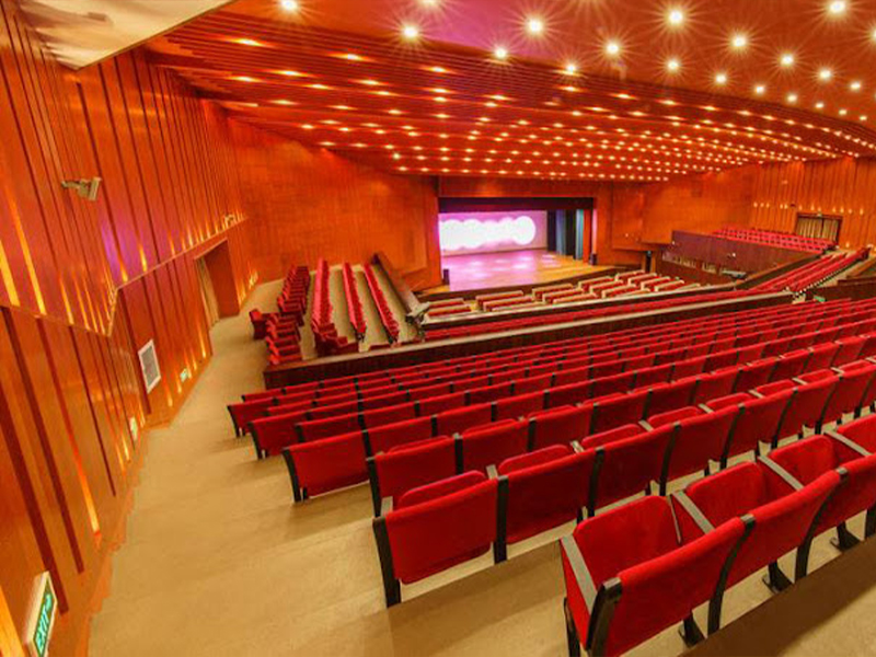 Modern Auditorium With Red Seating and Wood Panel Decor Modern auditorium with red seats, wood paneling, stage lighting, and empty seating for events.