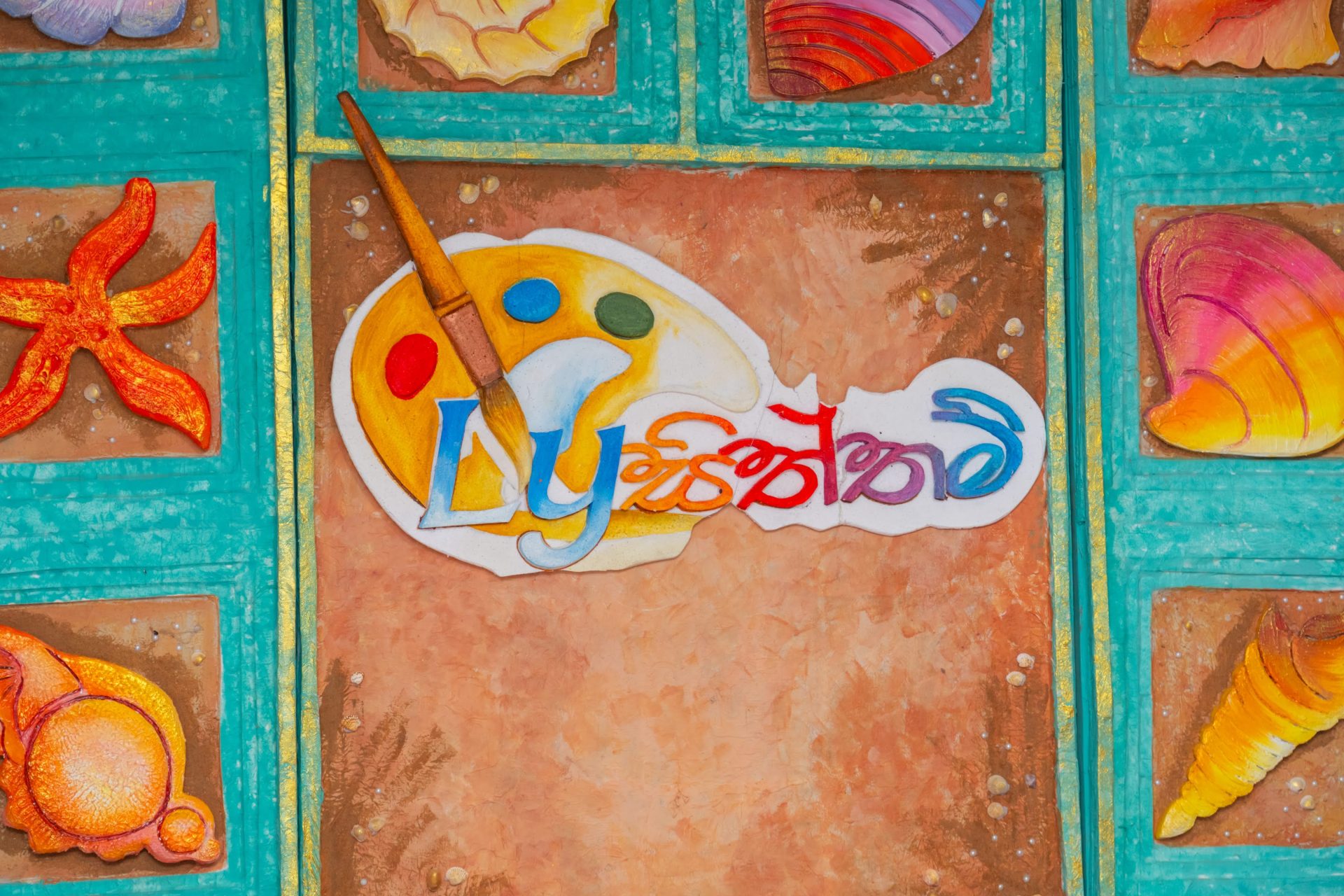 Colorful mosaic panel with artist’s palette, paintbrush, starfish, and seashells on a sandy background.