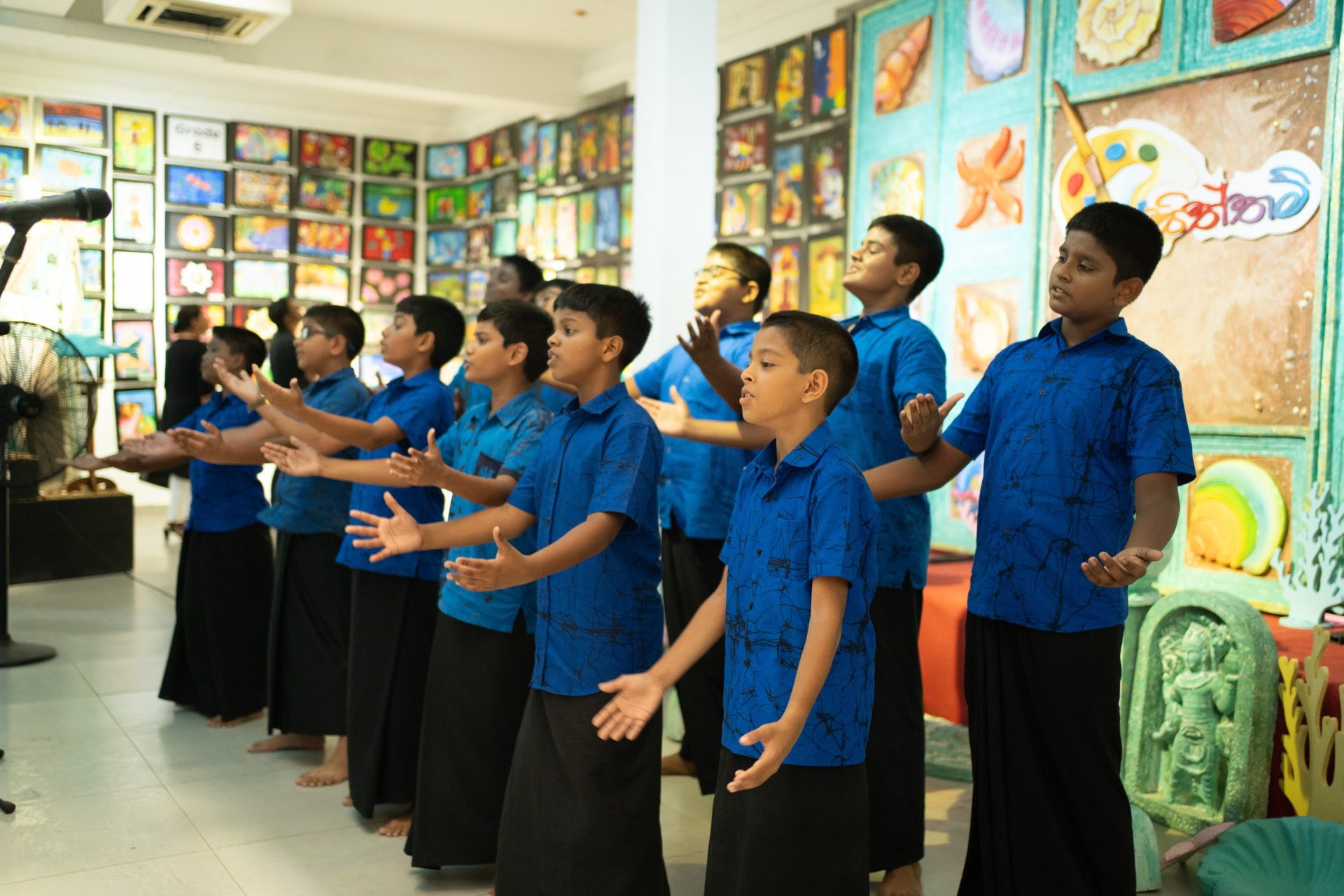 Boys choir in blue shirts performs traditional dance at vibrant indoor school art festival.