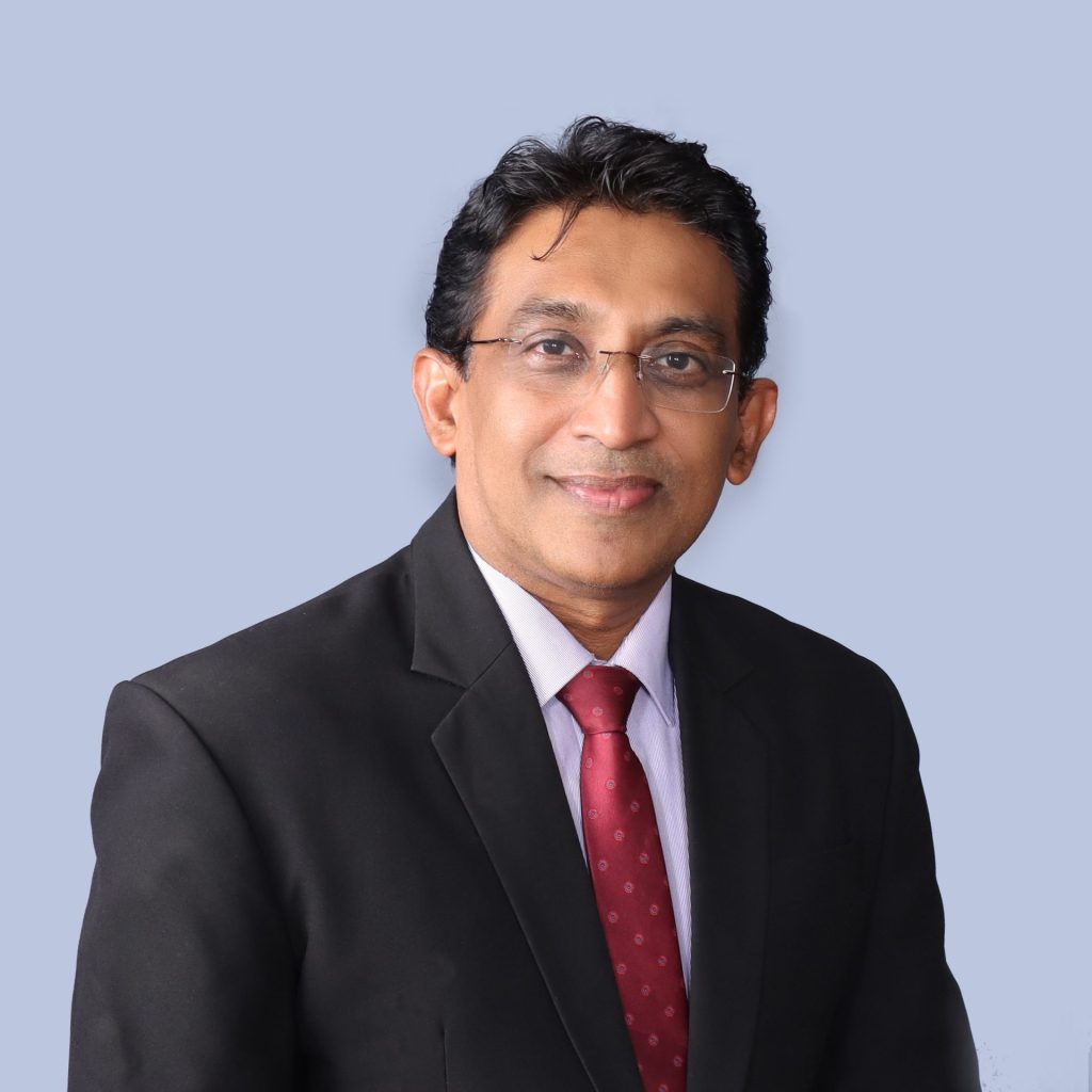 Professional headshot of Madhura Loku Kaluge in business attire, blue background, confident and friendly.