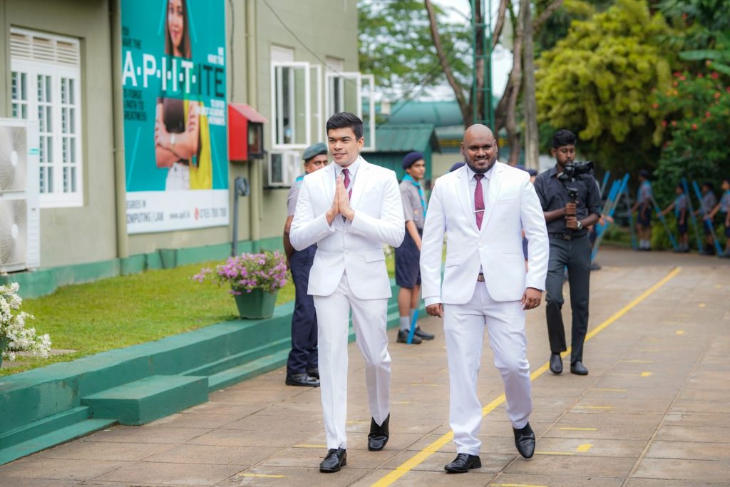 Two men in white suits lead a formal event at an educational campus with scouts present.