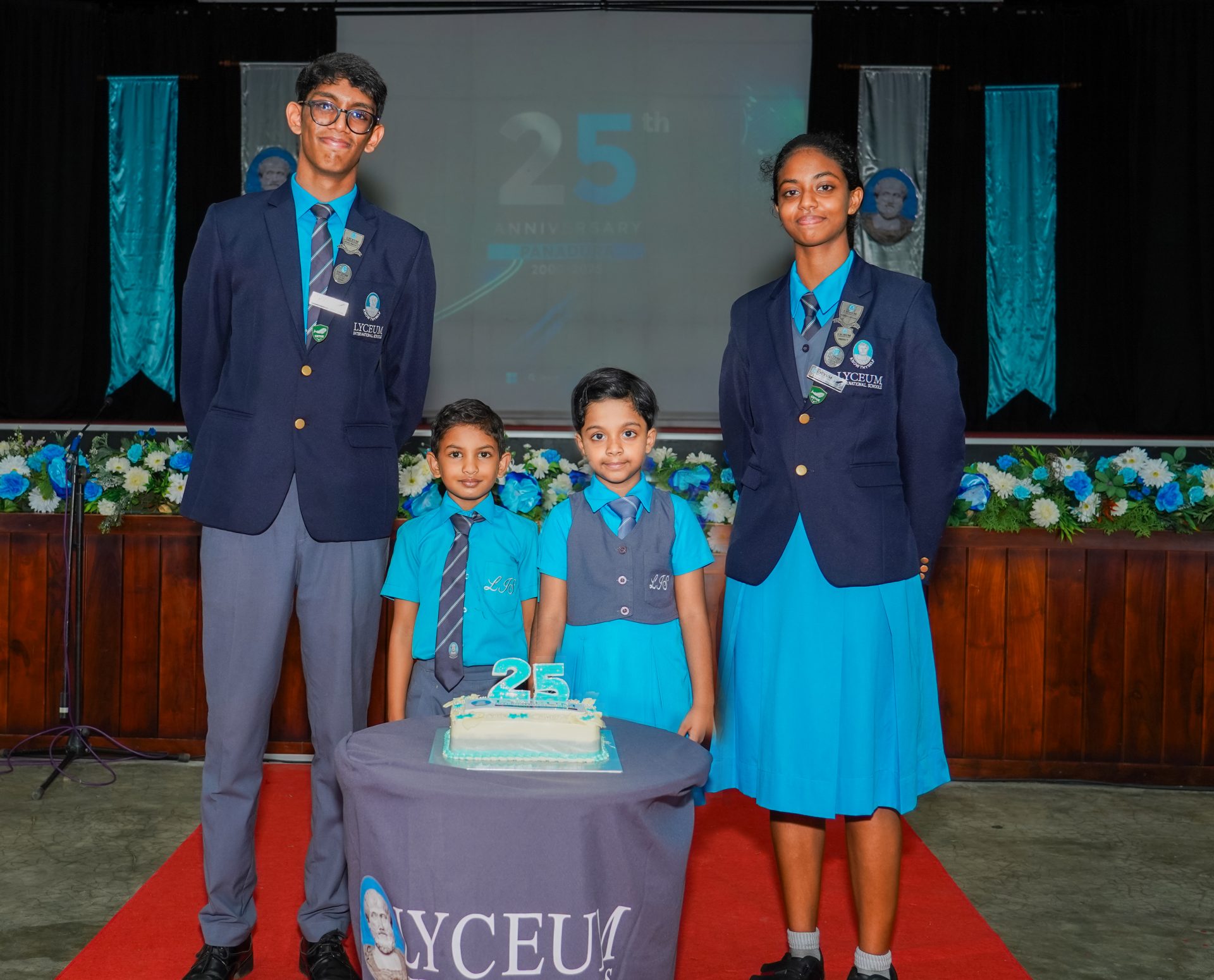 Lyceum Students Celebrate 25th Anniversary With Cake and Unity Lyceum school students celebrate 25th anniversary with cake, uniforms, and festive decorations indoors.