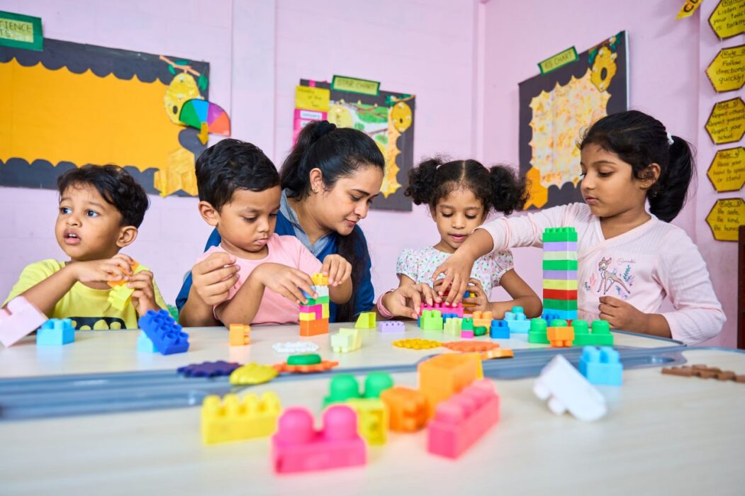 Preschool classroom with children and teacher building blocks, early childhood education, Lyceum Leaf School.