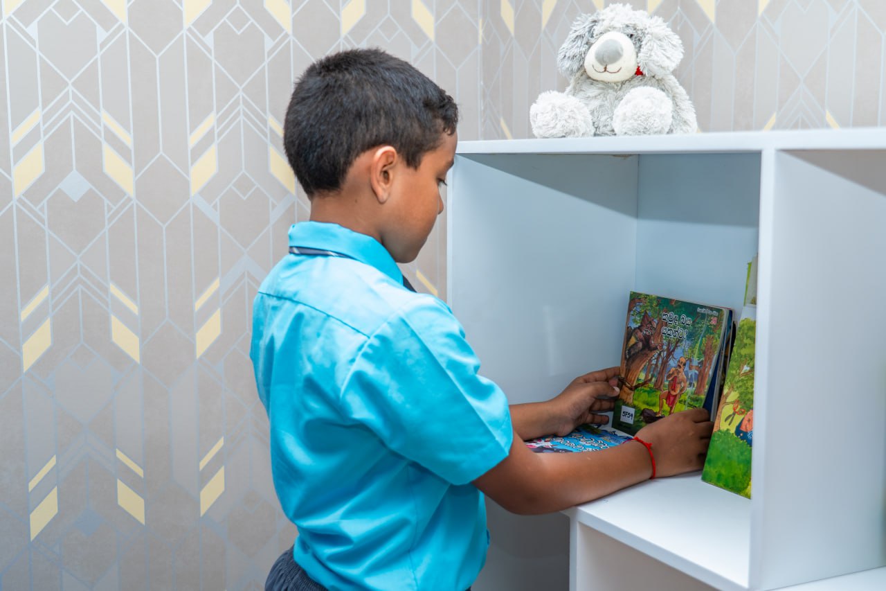 Young boy in school uniform choosing books from a white bookshelf in a modern children’s room.
