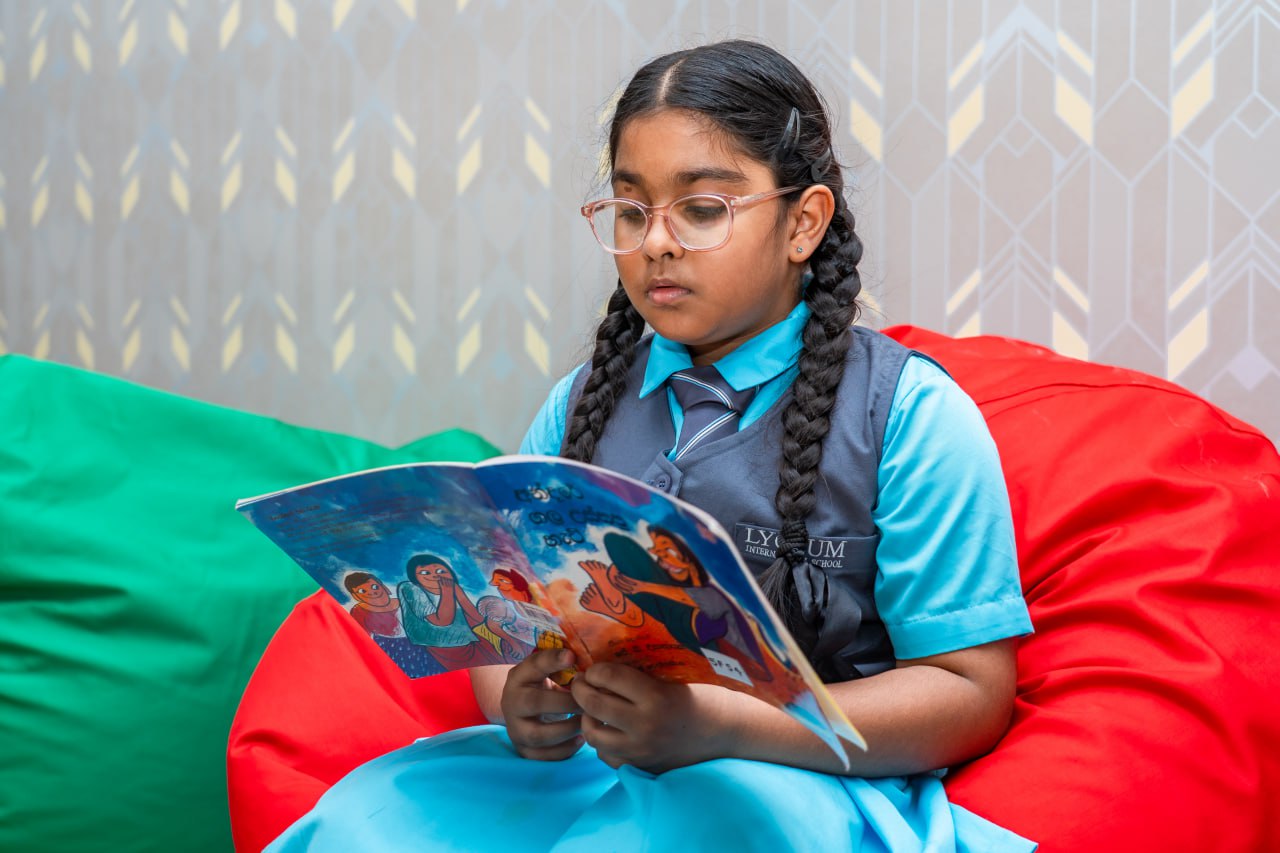 Schoolgirl reading illustrated book on bean bag at Lyceum International School library.