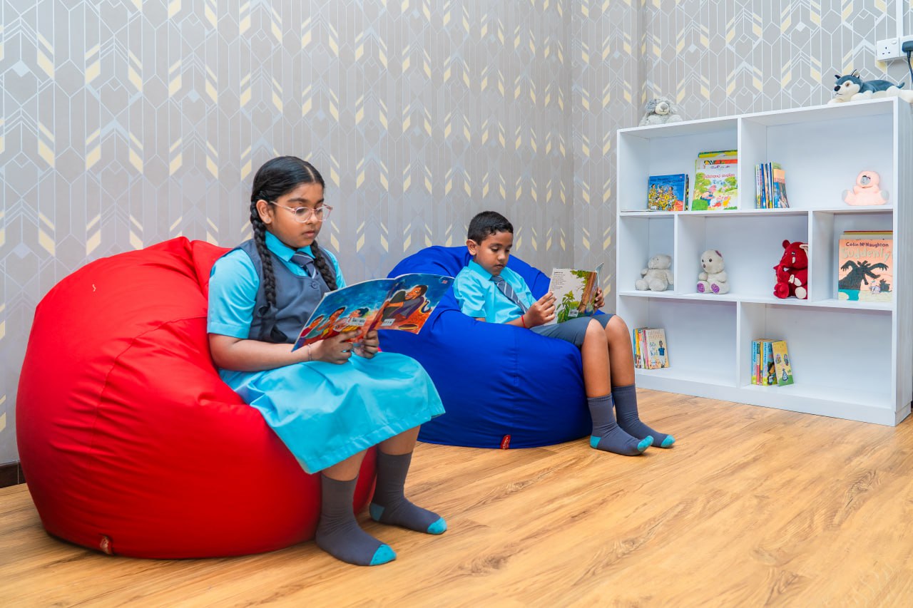 Children reading books on bean bags in a cozy classroom reading corner with plush toys.