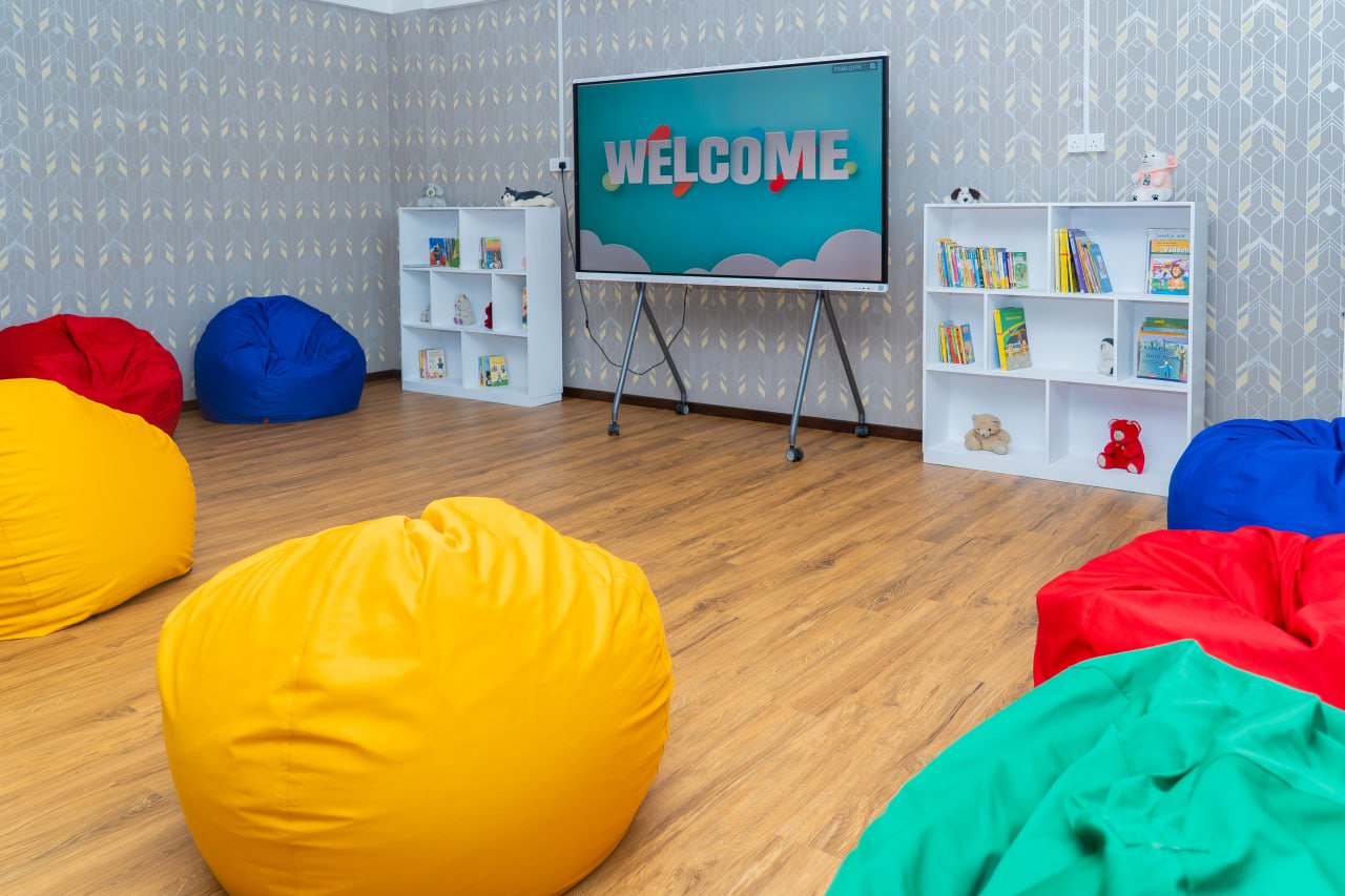 Modern childrens reading room with colorful beanbags, bookshelves, toys, and interactive display screen.