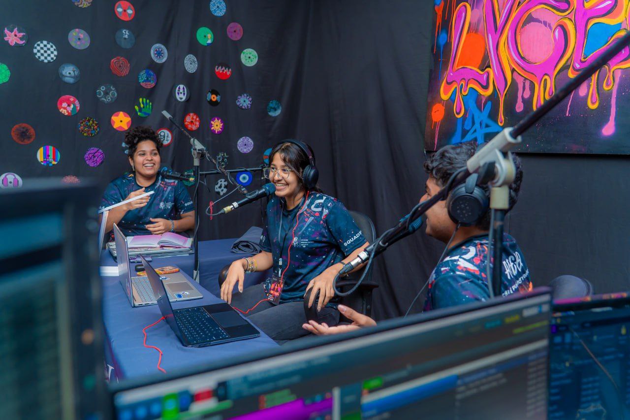 Young podcasters recording a youth radio show with microphones, laptops, and colorful creative background.