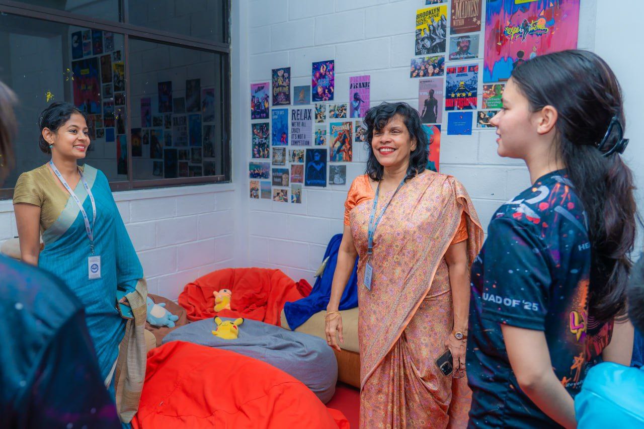Students and teachers chatting in a colorful, poster-filled lounge with bean bags and pop culture decor.