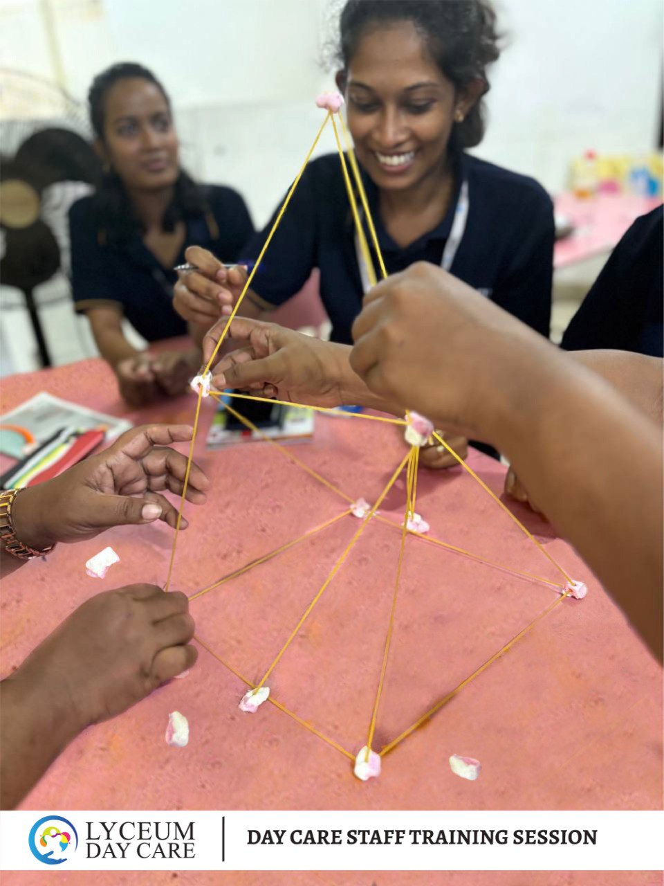 Day care staff build spaghetti marshmallow tower during team-building training activity.