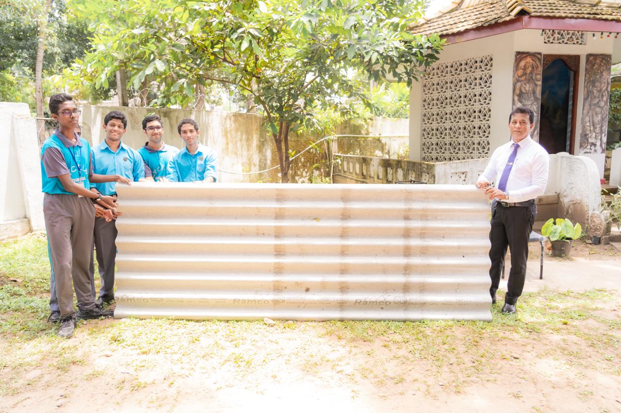 Students and teacher present Ramco corrugated sheet at school donation event outdoors.
