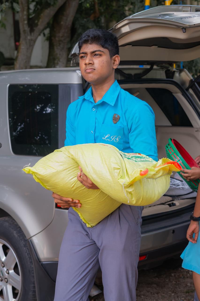 Student in blue uniform carries heavy yellow sack during outdoor community service activity.