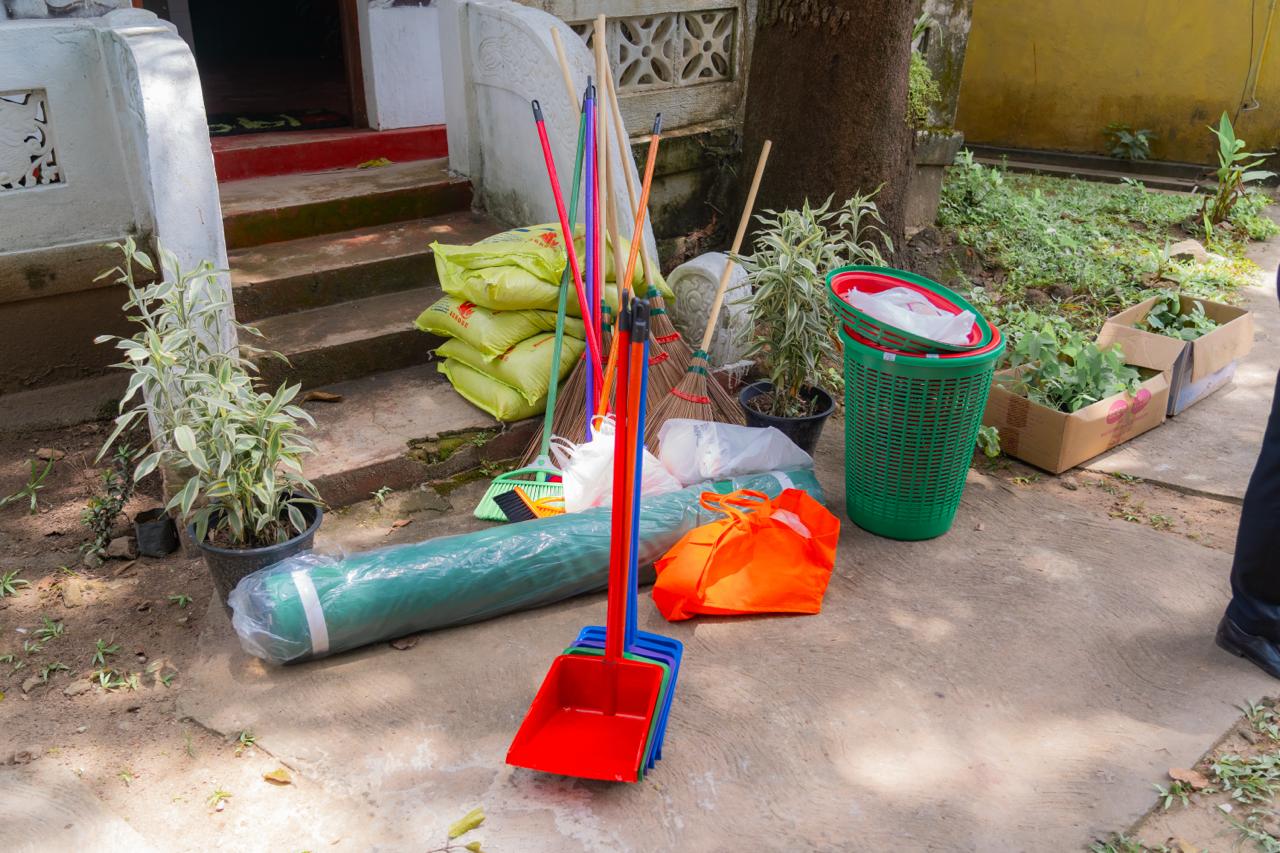 Community gardening tools, cleaning supplies, dustpans, brooms, and plants organized outdoors for cleanup event.