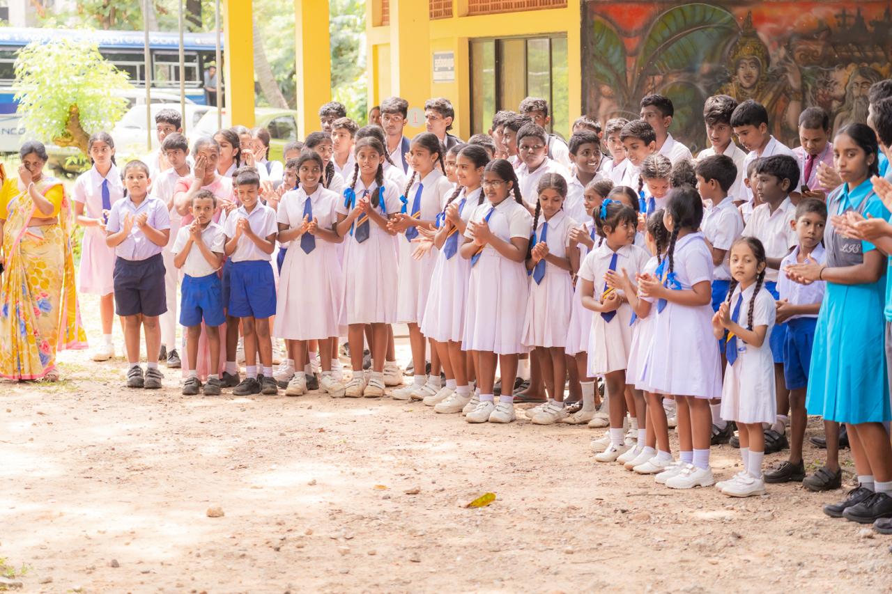 Indian school children in uniforms at outdoor assembly, clapping and celebrating with teachers present.
