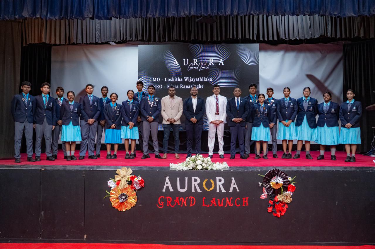 Formal group photo at Aurora Grand Launch event with students, faculty, and festive stage decorations.